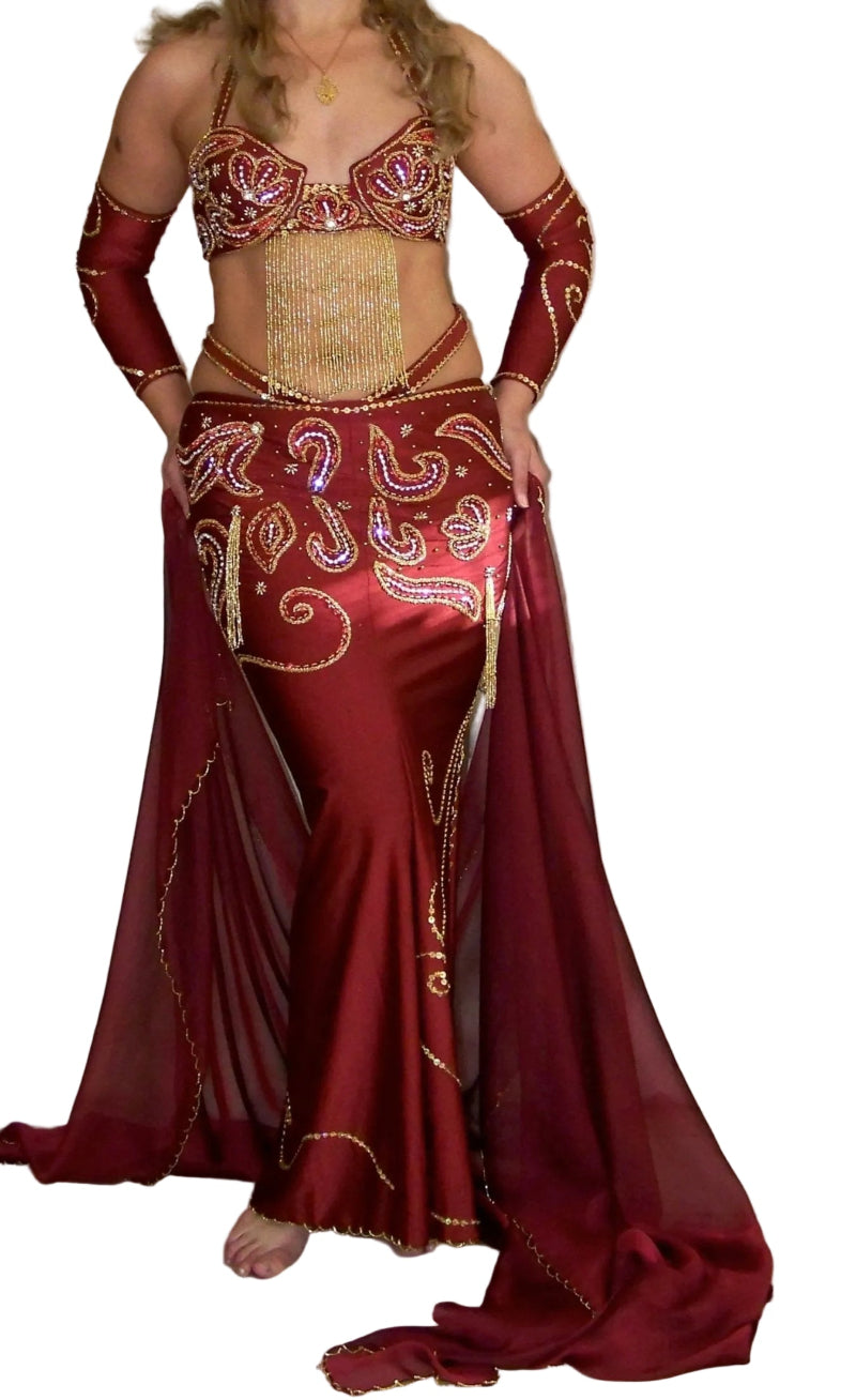 A woman modeling a professional red belly dance costume with a bra, skirt, and decorations.