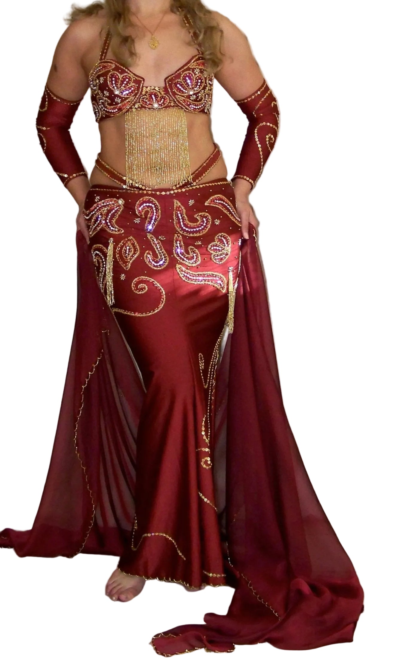 A woman modeling a professional red belly dance costume with a bra, skirt, and decorations.