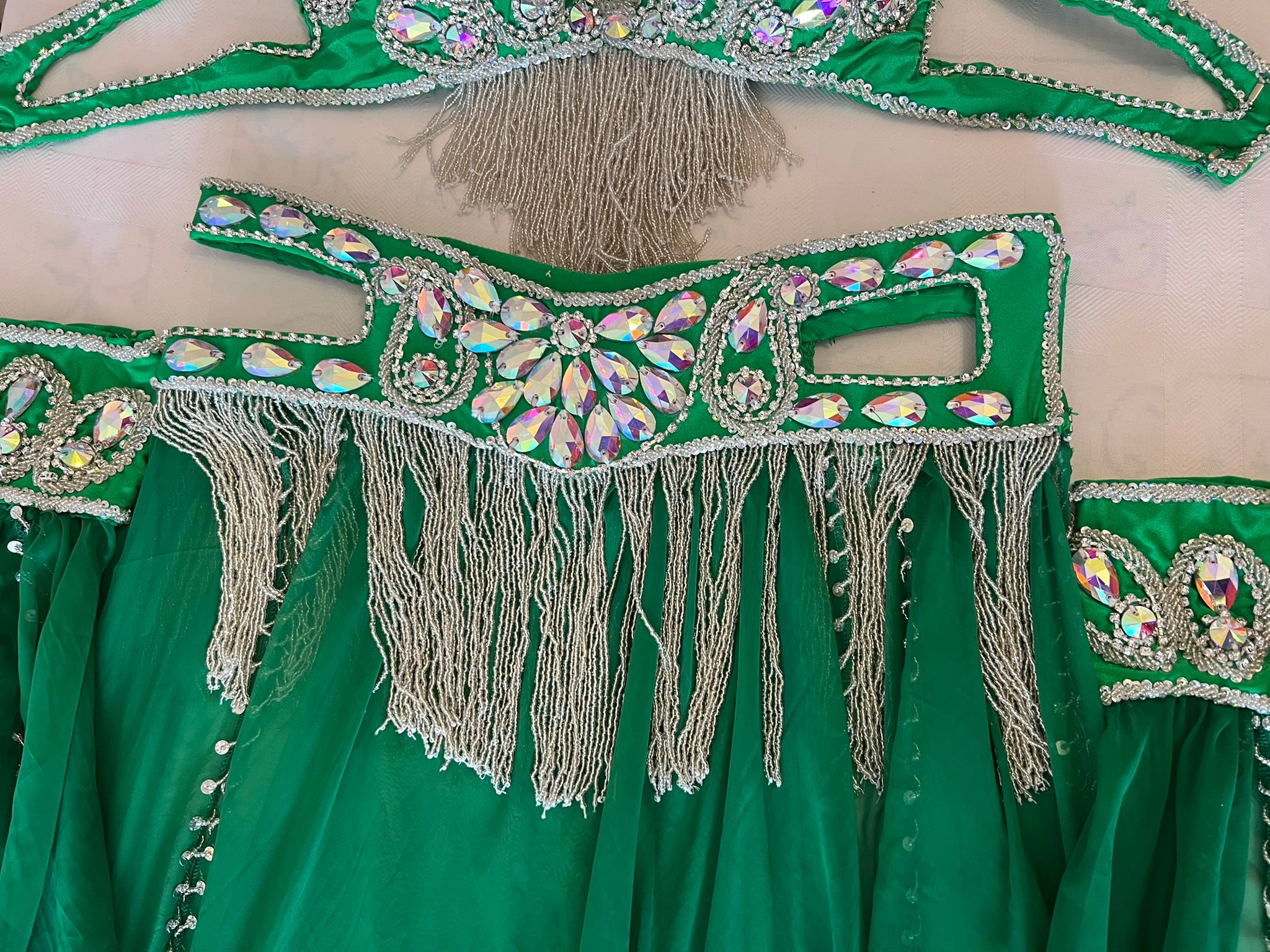 Green embroidered garment with silver fringes and embellishments on a beige background