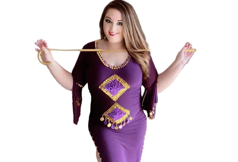 A woman in a purple belly dance dress with embroidered sequins, posing in a room with a blurred background.
