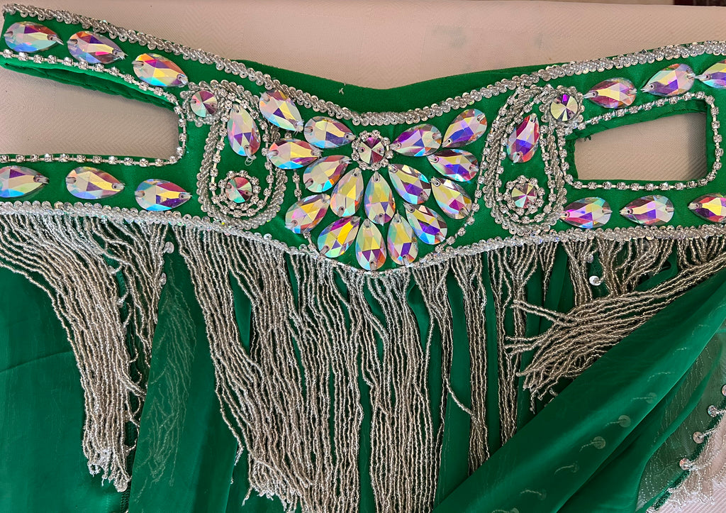 Green fabric with decorative embellishments featuring crystals and fringes on a beige background.