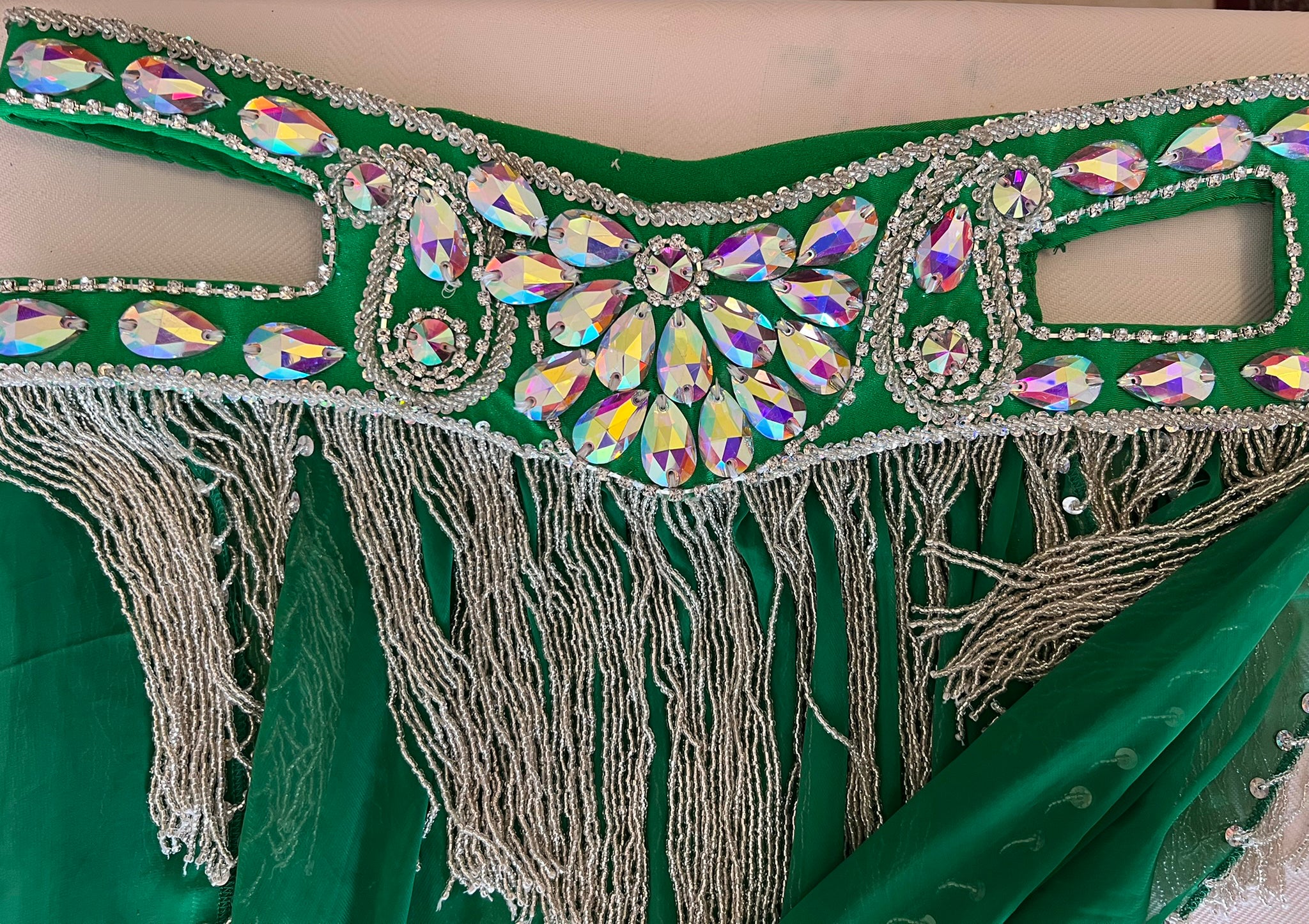 Green fabric with decorative embellishments featuring crystals and fringes on a beige background.