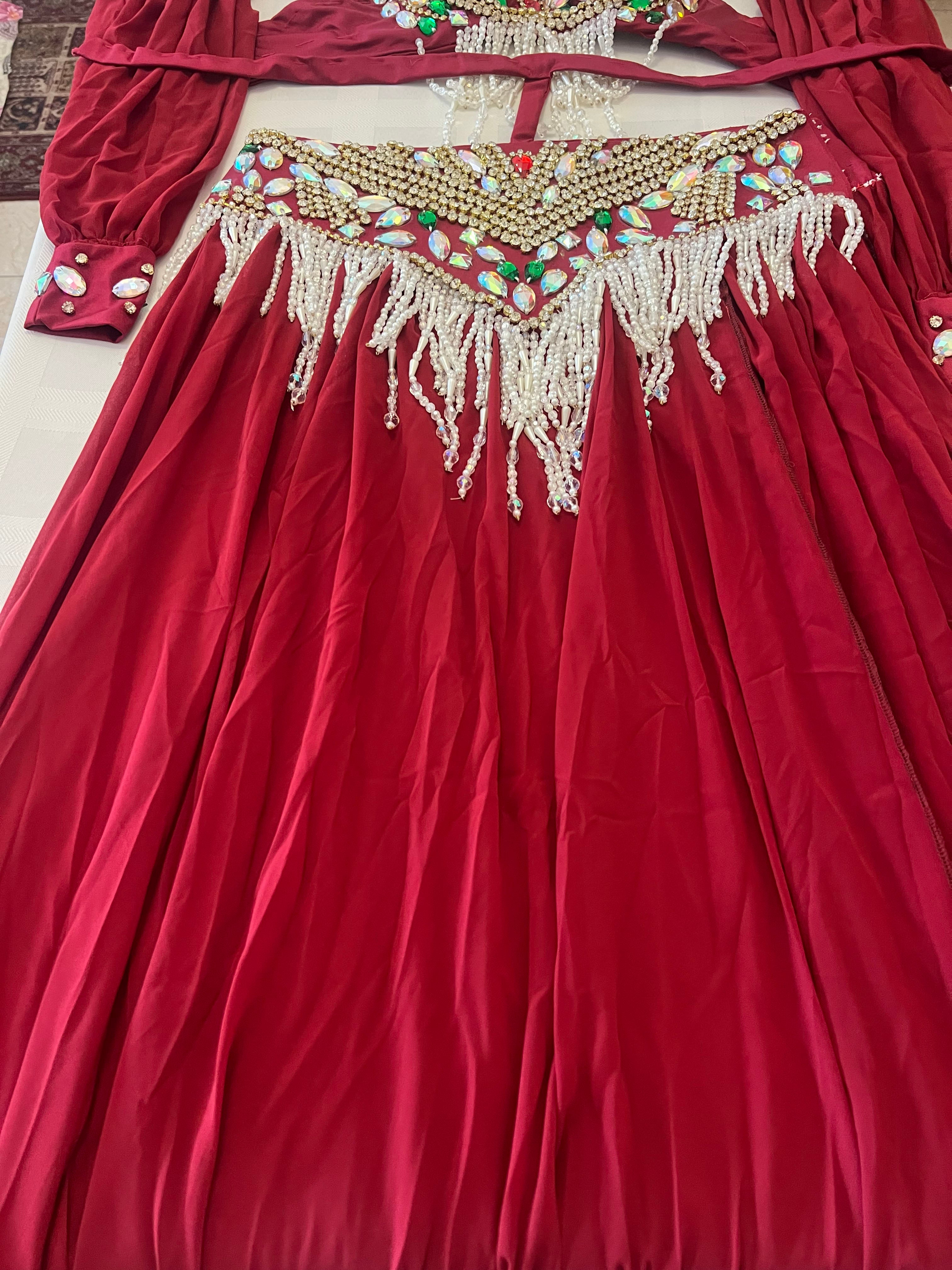 A red traditional dress with a heavily embellished gold, silver, and multicolored beaded waistband and white fringe, laid flat on a light surface.