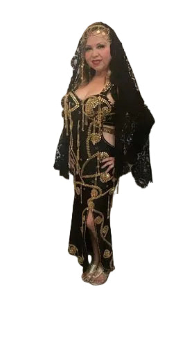 Woman in a black and gold dress standing in a decorated room with flowers and a mirror.