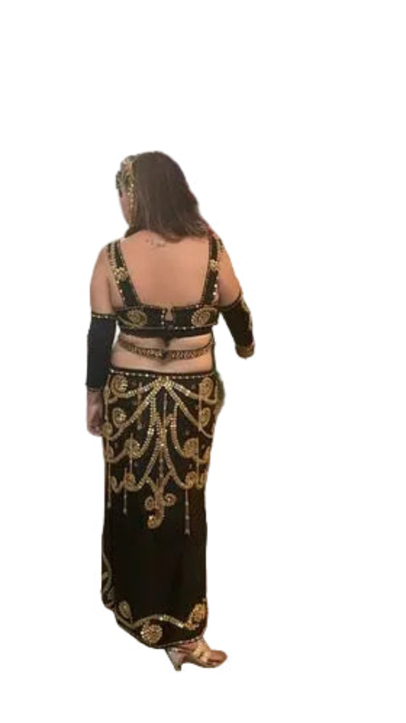 Woman in a black and gold traditional outfit standing in a room with floral decorations.