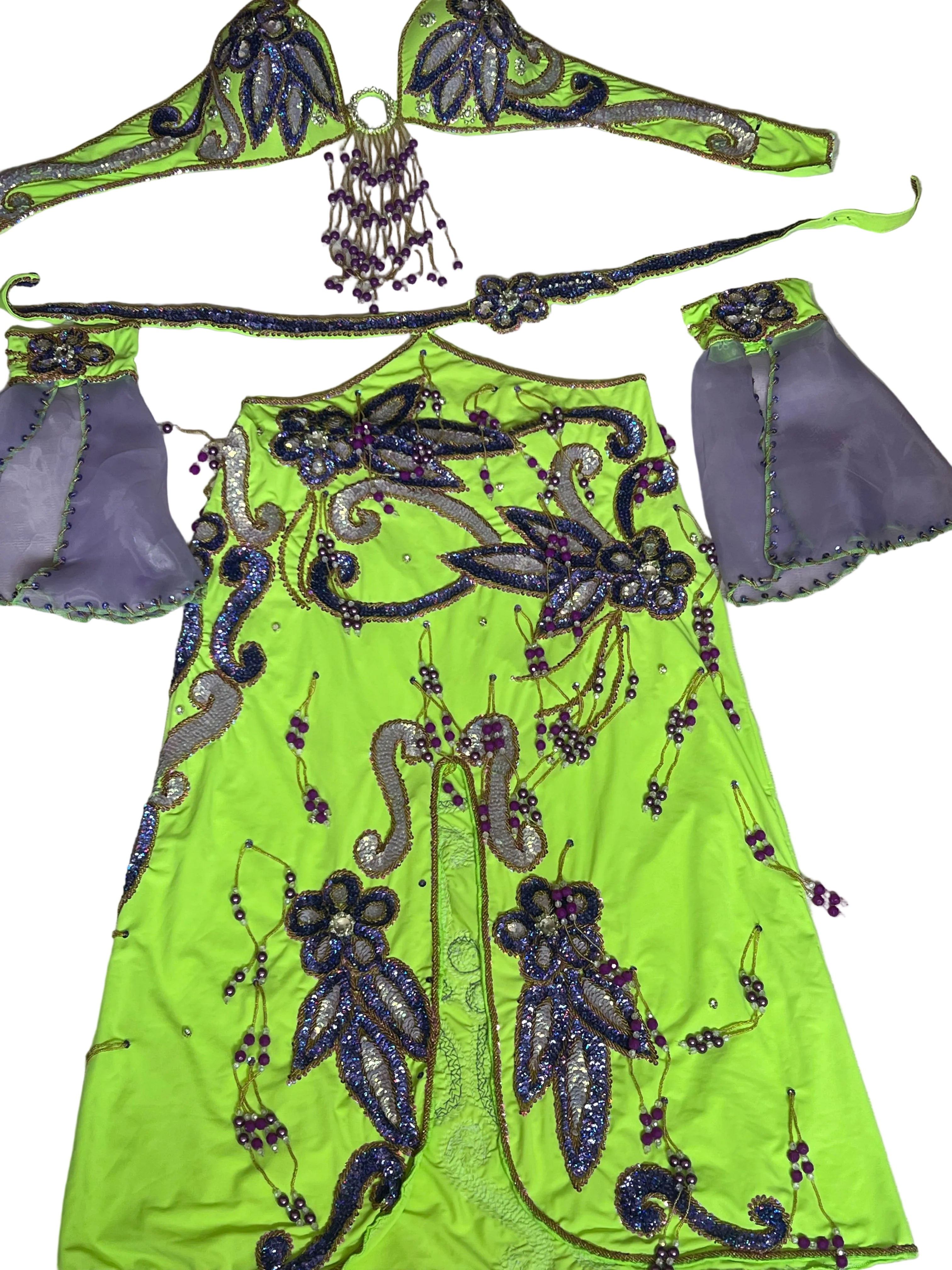 A neon yellow-green embellished costume dress laid flat on a light fabric surface, with matching accessories including a headpiece, belt, and sleeve pieces in lavender and purple beaded embroidery.