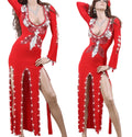 A model wearing a red belly dance dress with embellishments and a V-neckline, posed in a room with a white bed and a mirror in the background.