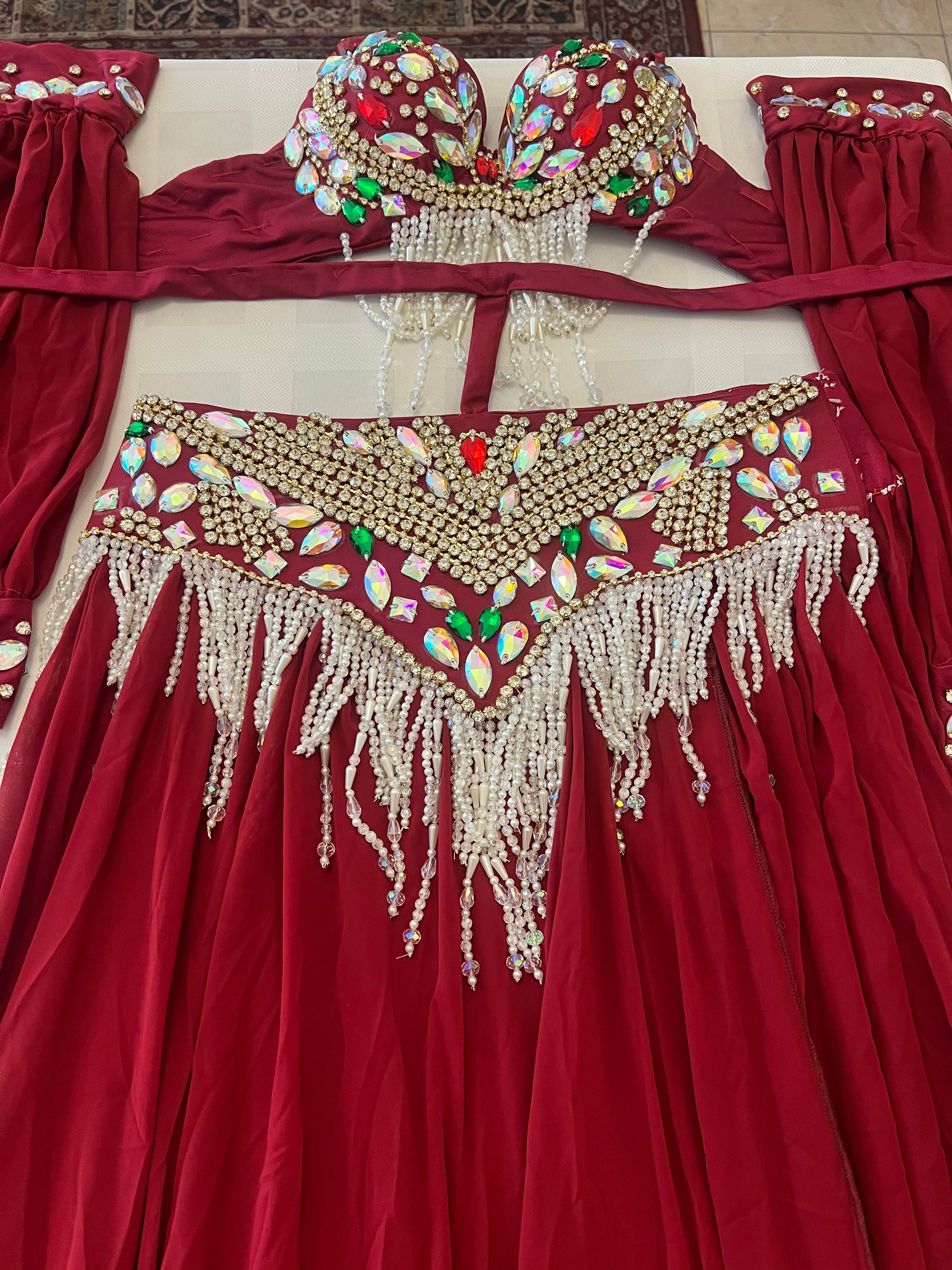 A deep red belly dance dress with extensive gold, white, and multicolor beadwork and embellishments, laid flat on a light-colored surface.