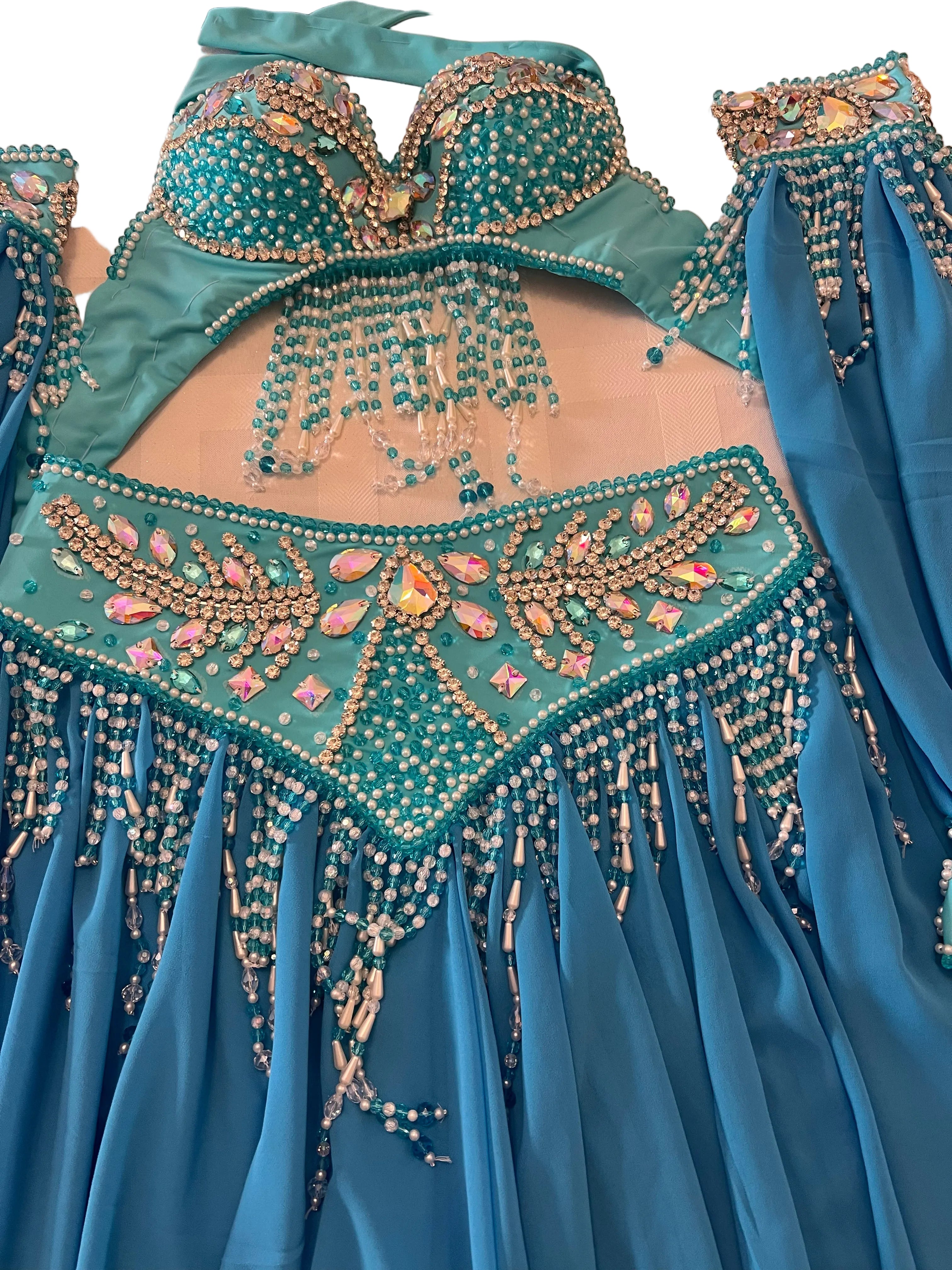 A turquoise belly dance costume set featuring a beaded bra top with dangling bead chains, a matching embellished waistband, and a flowing blue skirt, laid flat on a light surface.
