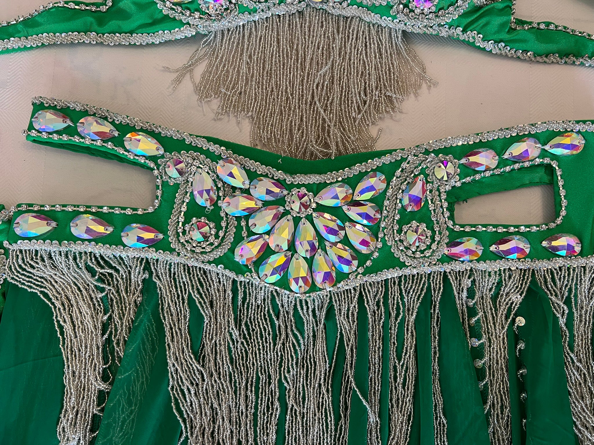 Green costume with decorative elements and tassels on a beige background