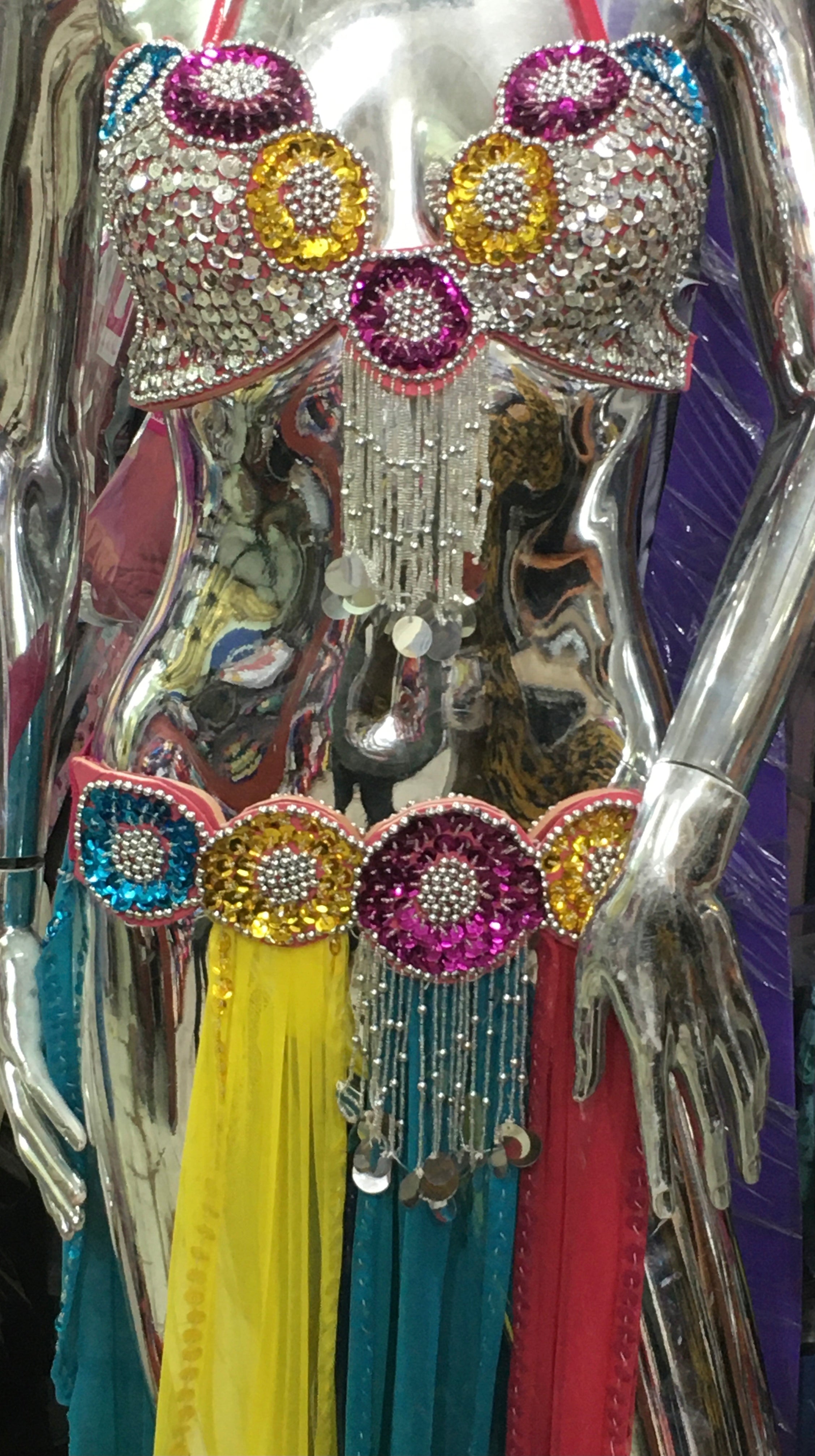 A professional belly dance costume displayed on a mannequin, featuring a multicolored embroidered bra, a rigid belt with attached tulle skirt, and a small tulle scarf for shoulder decoration.