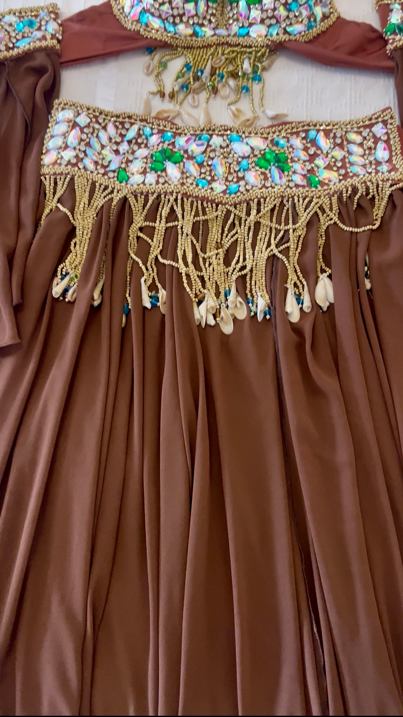 Close-up of a brown satin dress with gold beaded fringe and embellished neckline details, showing pleated fabric and decorative trim.