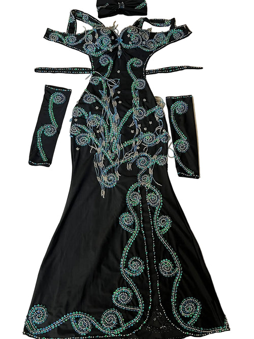 A custom-made belly dance costume laid out on a flat surface, consisting of a black one-piece dress with green embellishments, arm pieces, and a headpiece.