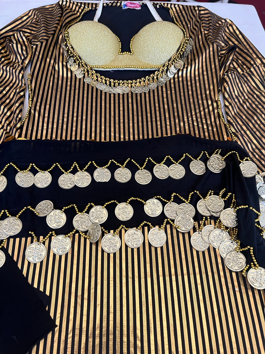 A belly dance outfit with a black and gold striped dress, a matching bra, and a scarf, adorned with handmade embroidery and metal accents.