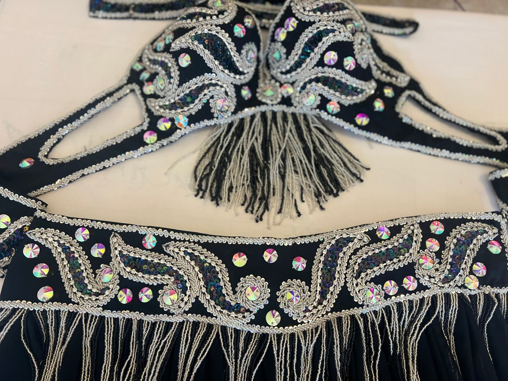 Decorative belt with intricate patterns, rhinestones, and fringes on a black background