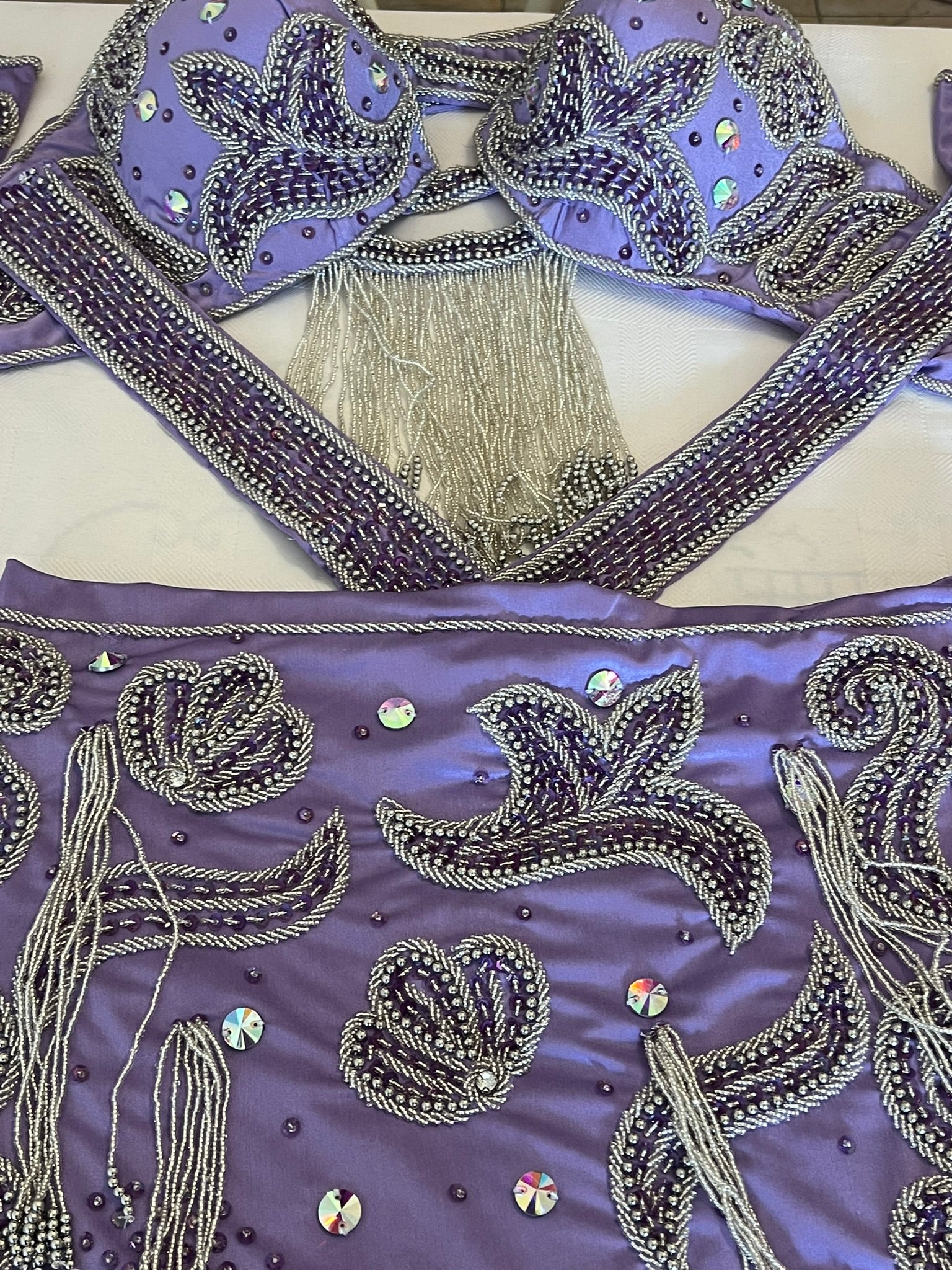 Decorative purple fabric of belly dance costume with intricate silver embroidery and embellishments on a white background