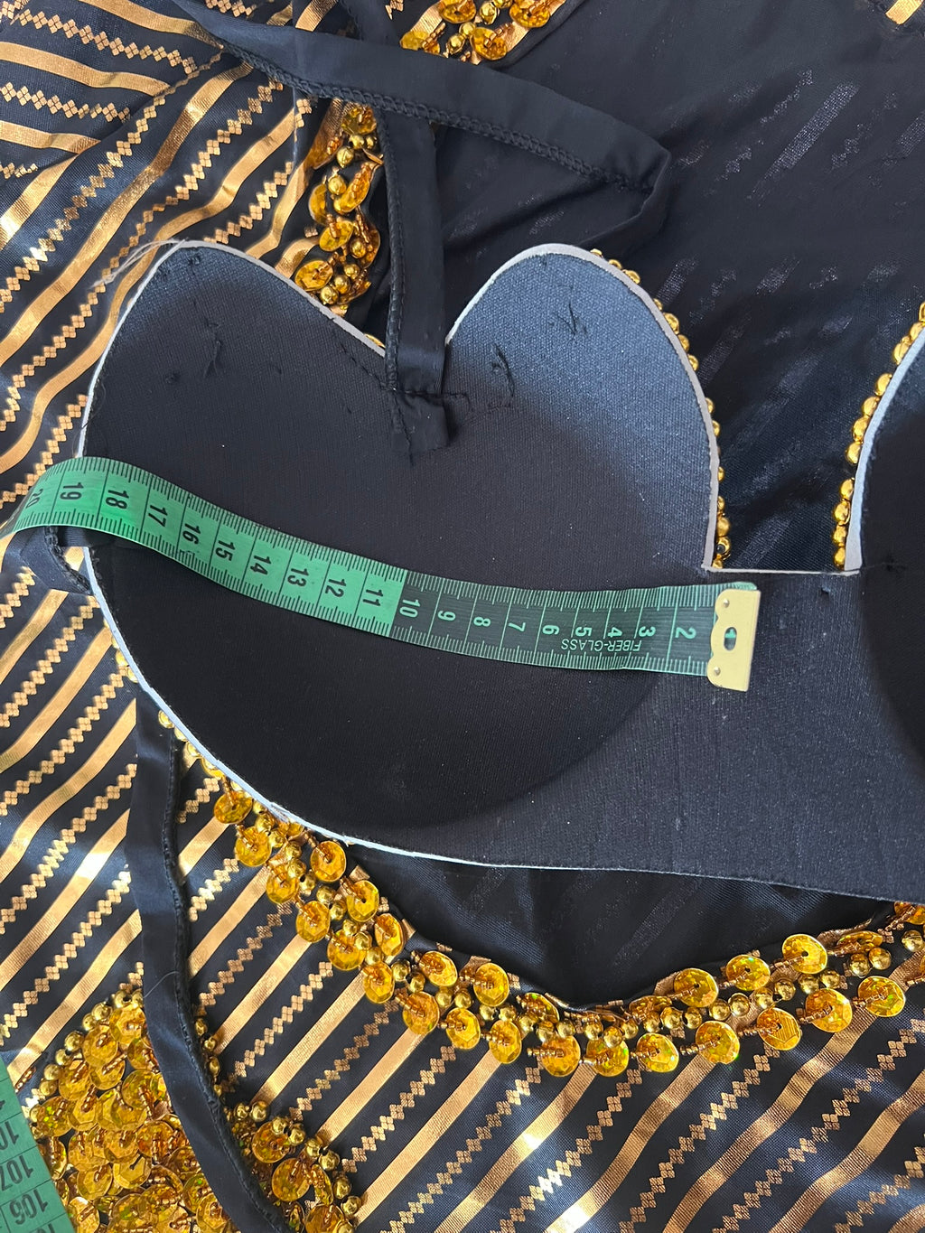 Black blouse with gold embroidery and a green measuring tape on a black and gold striped background