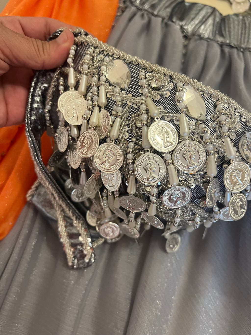 Decorative clutch with metallic coins and beads held by a hand against a gray background