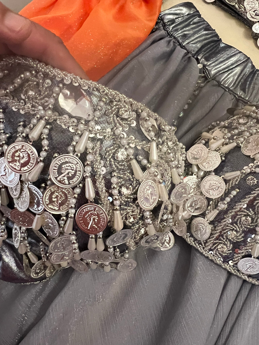 Close-up of a decorative fabric with coins and beads on a gray background