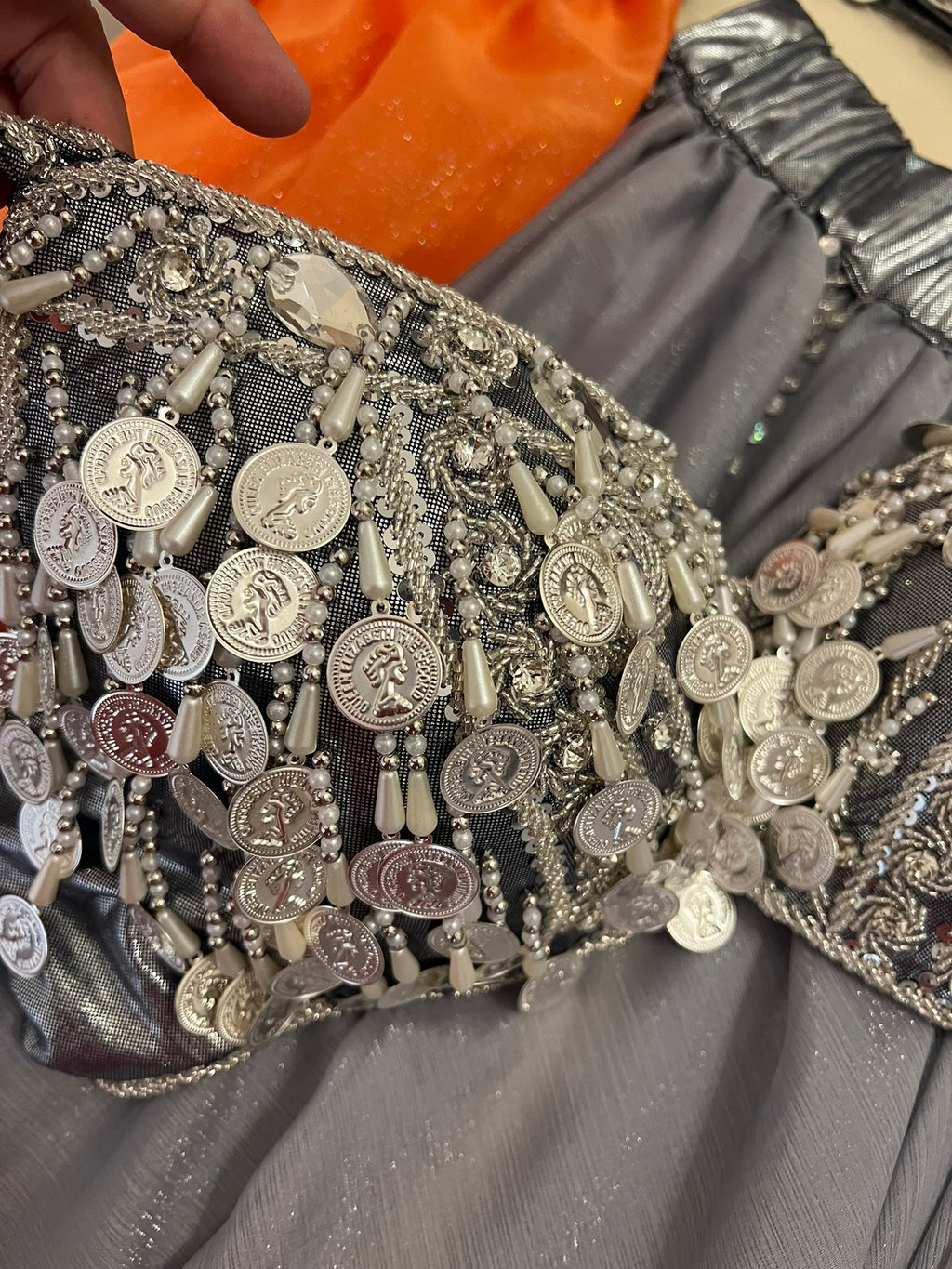 Close-up of a decorative garment with coins and beads on a gray fabric background.
