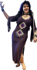 A woman in a purple belly dance costume with embellishments and a scarf, posing with one hand raised and a smile on her face.