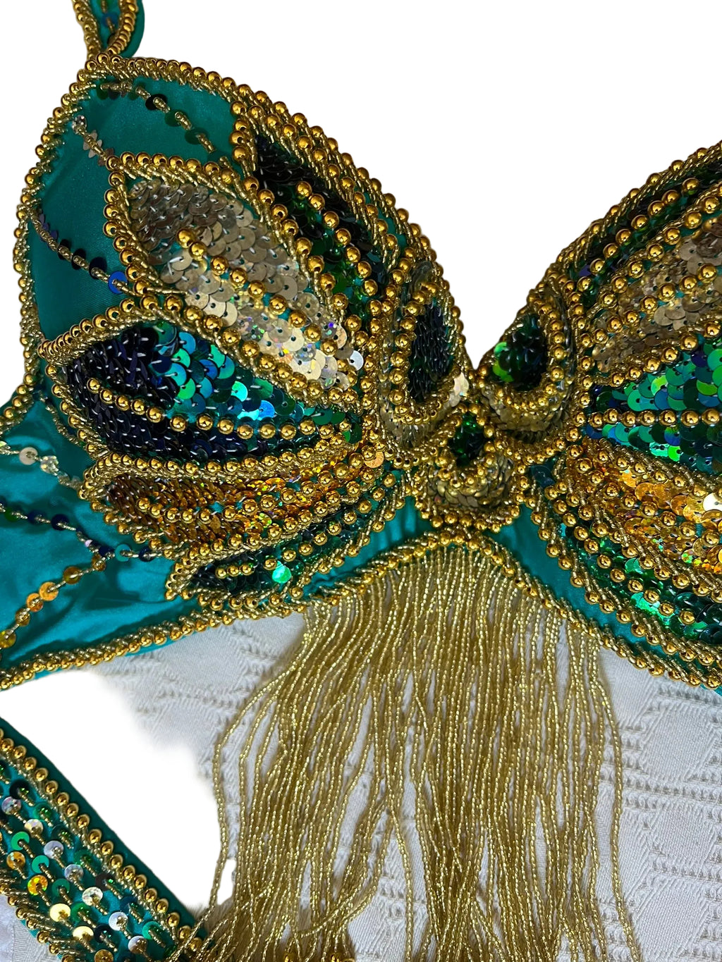 Close-up of a decorative belly dance bra with gold and green details on a textured white background