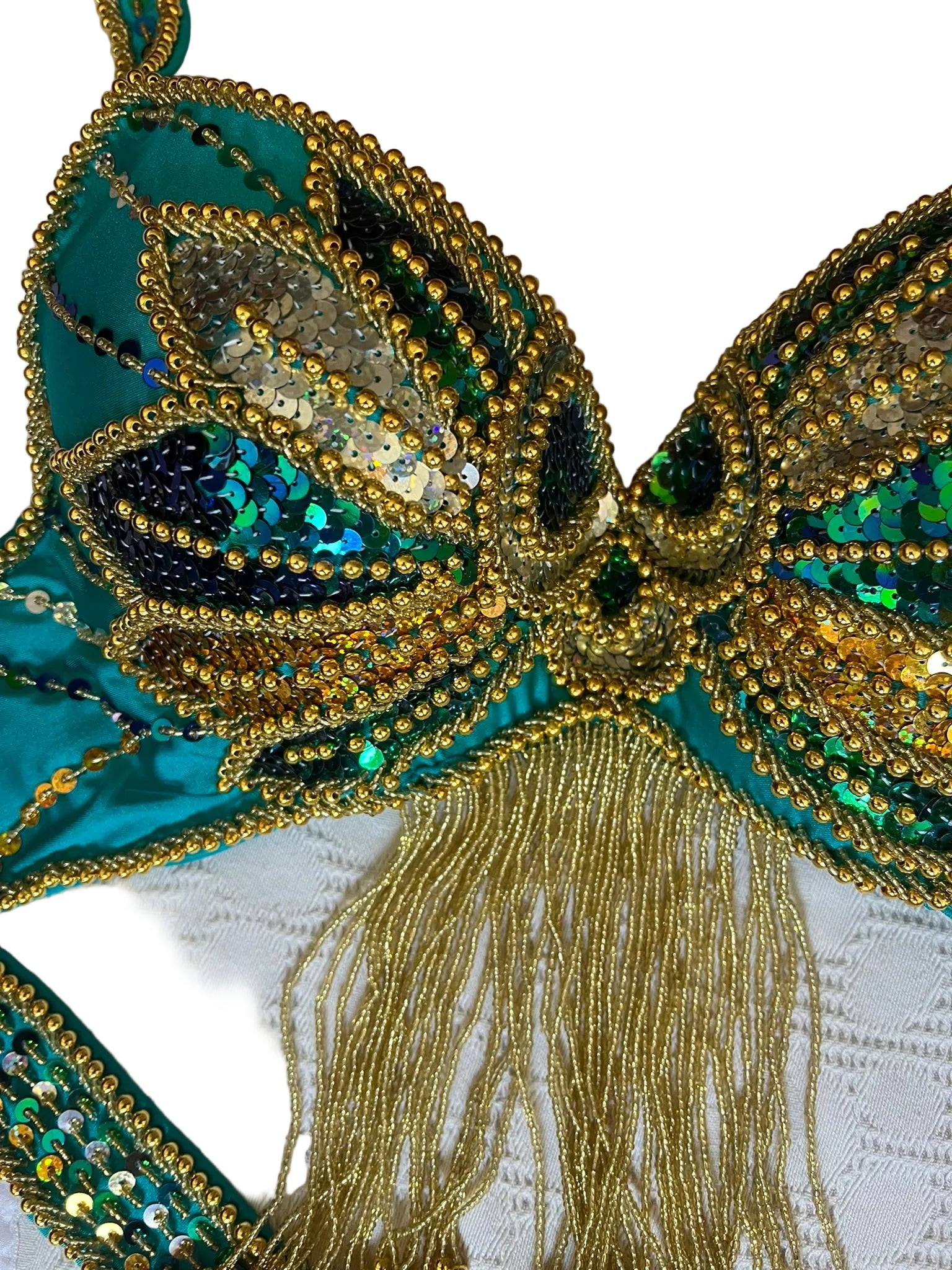Close-up of a decorative belly dance bra with gold and green details on a textured white background