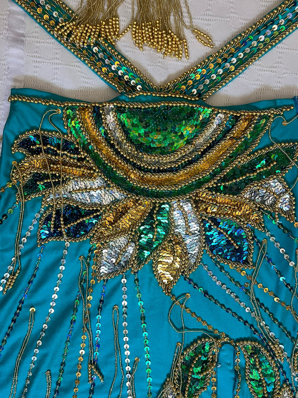 Close-up of a turquoise belly dance costume with gold, green, and silver beadwork