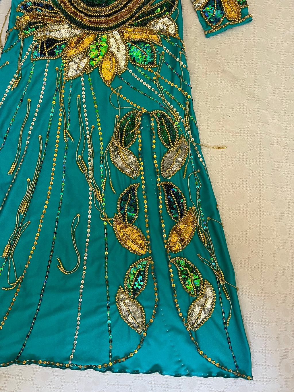 Teal fabric with gold and green bead embroidery on a beige background