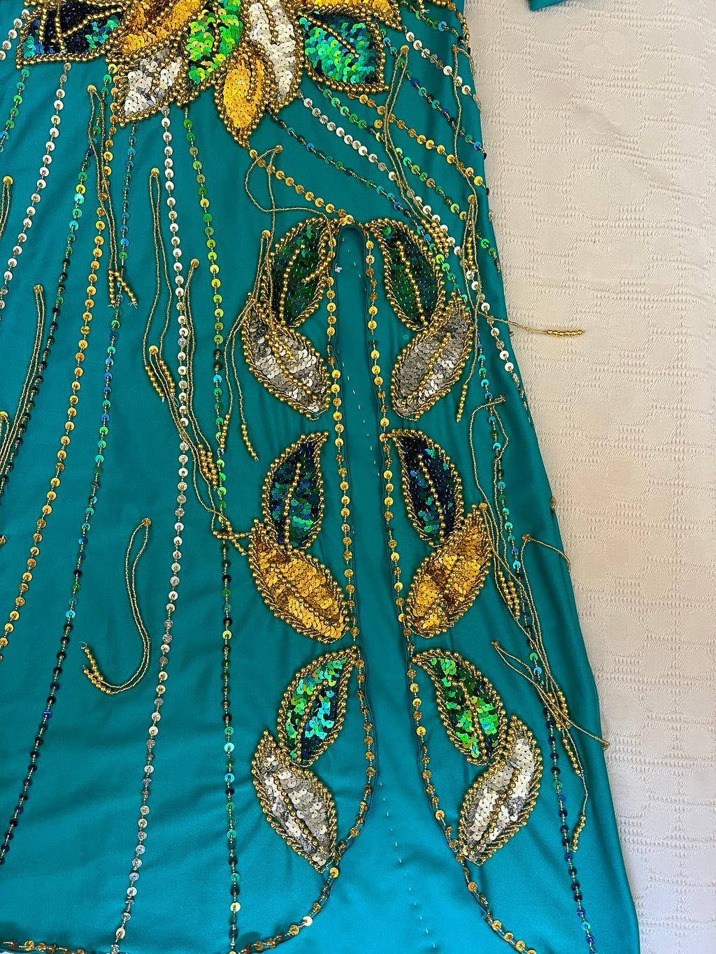Close-up of teal fabric with intricate gold, green, and silver beadwork.