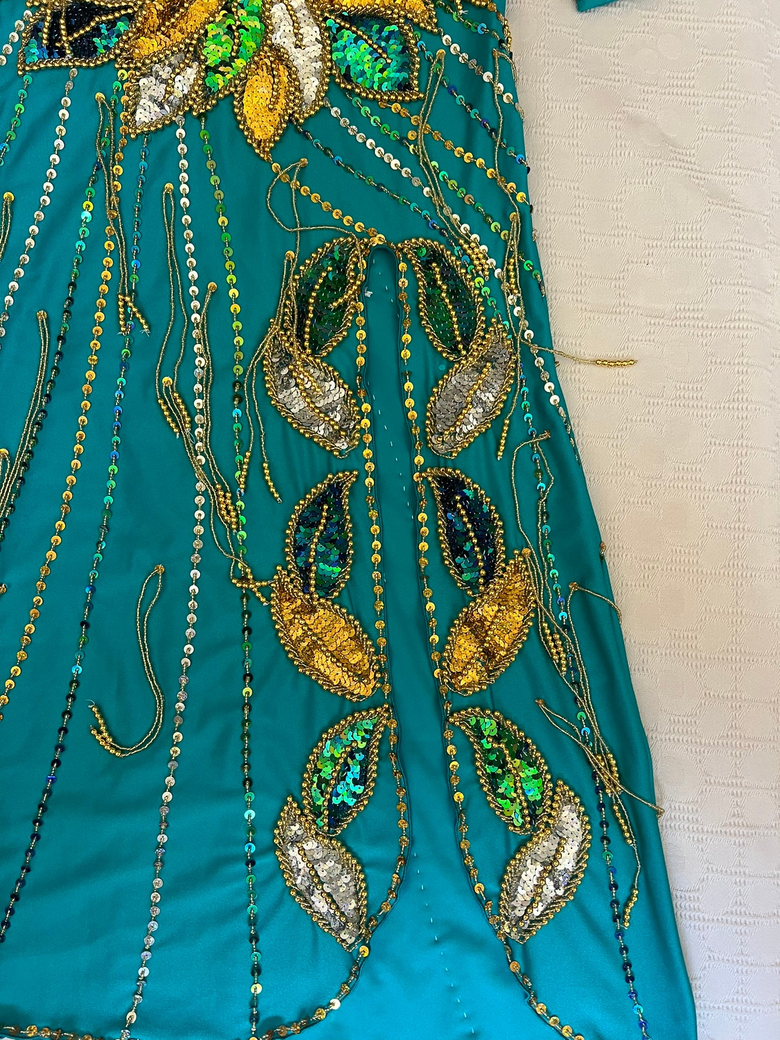 Close-up of teal fabric with intricate gold, green, and silver beadwork.