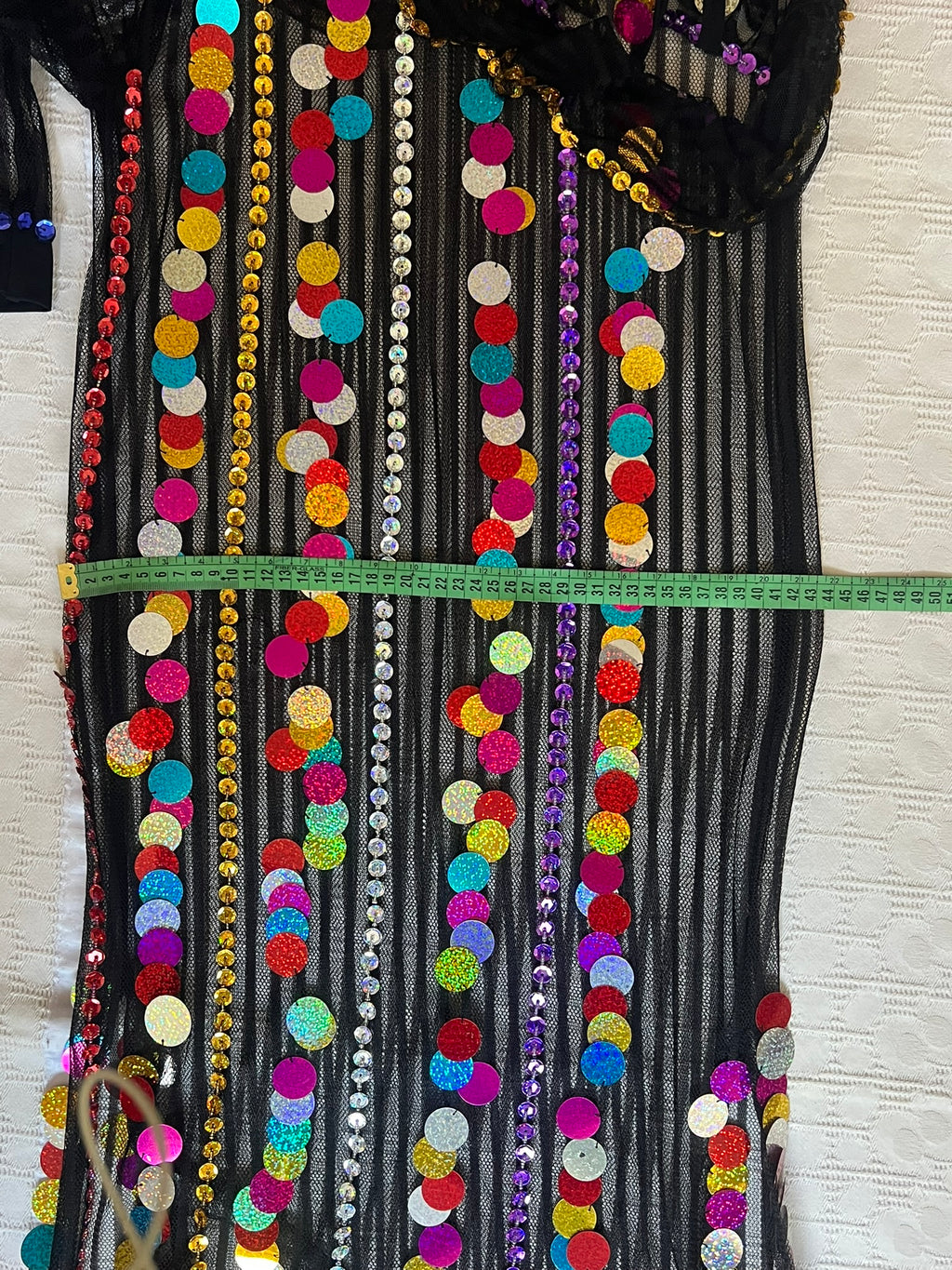 Decorative fabric with colorful sequins and beads, measured against a white wall.