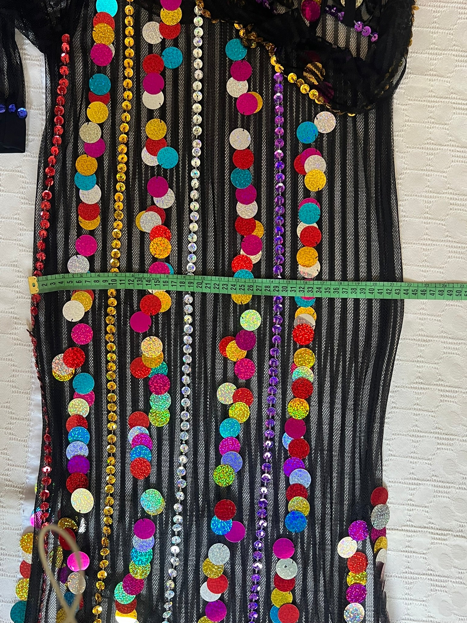 Decorative fabric with colorful sequins and beads, measured against a white wall.