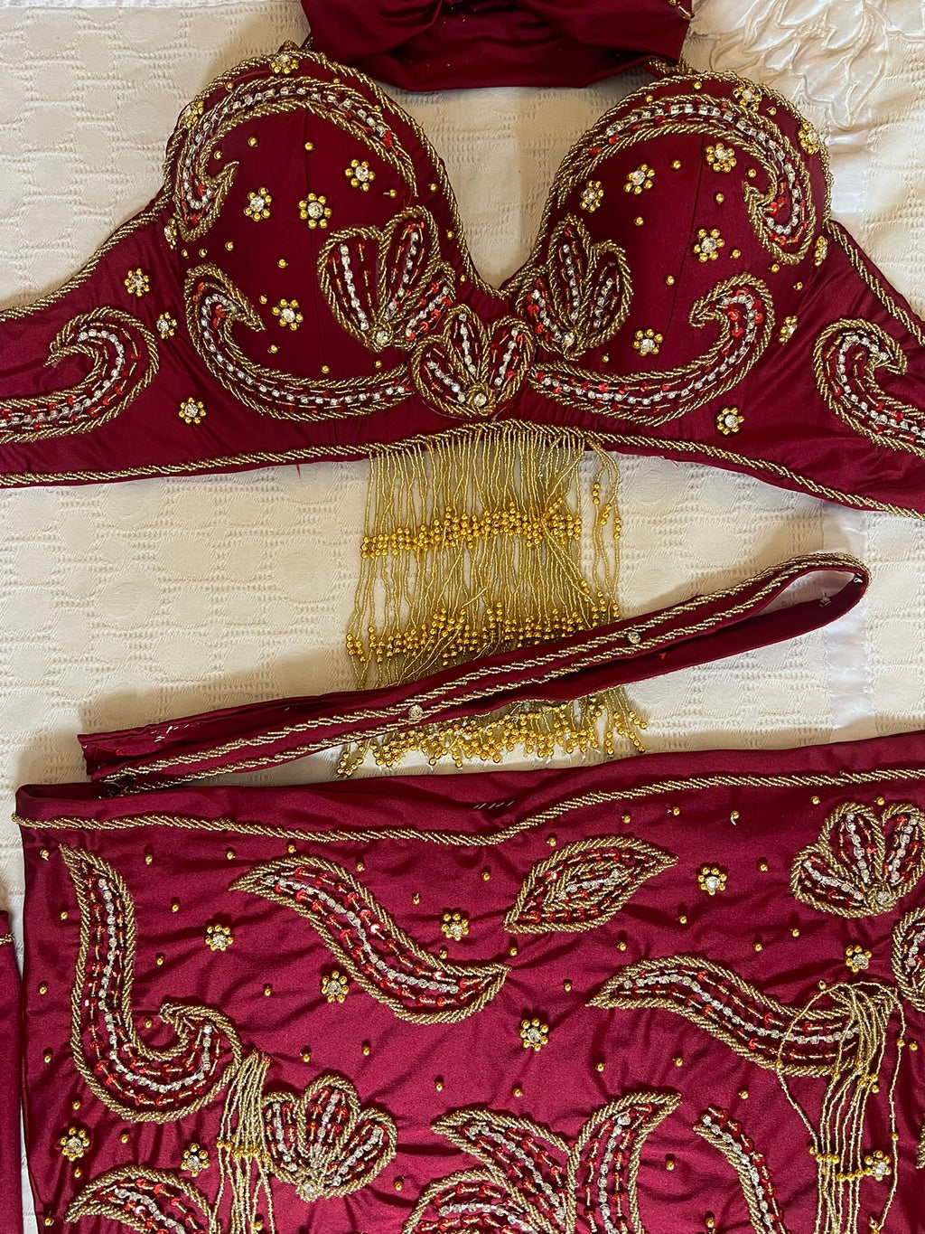 Red embroidered belly dance garment with gold detailing on a beige fabric background