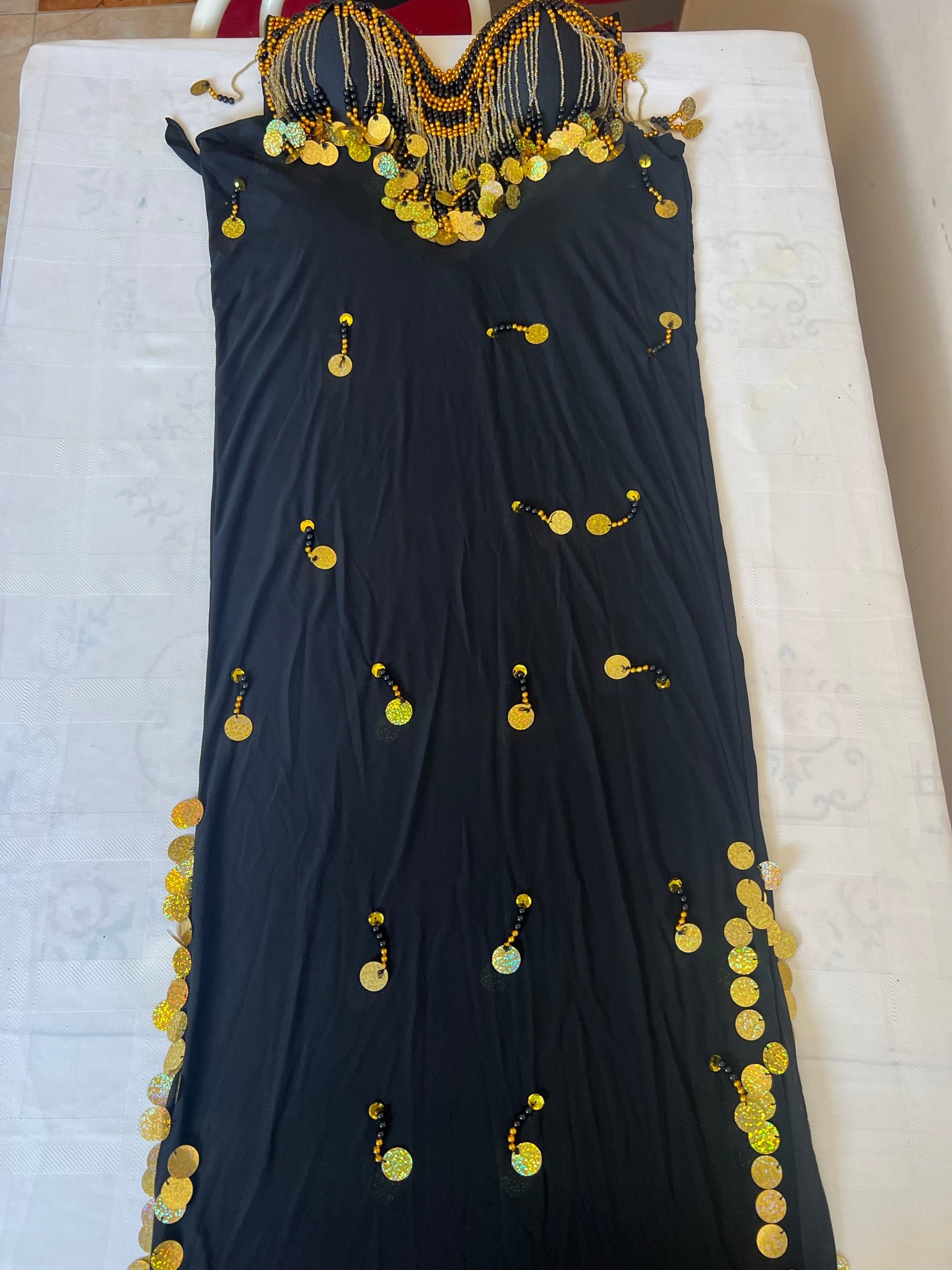 A black belly dance costume with handmade embroidered details and large sequins, displayed on a flat surface.