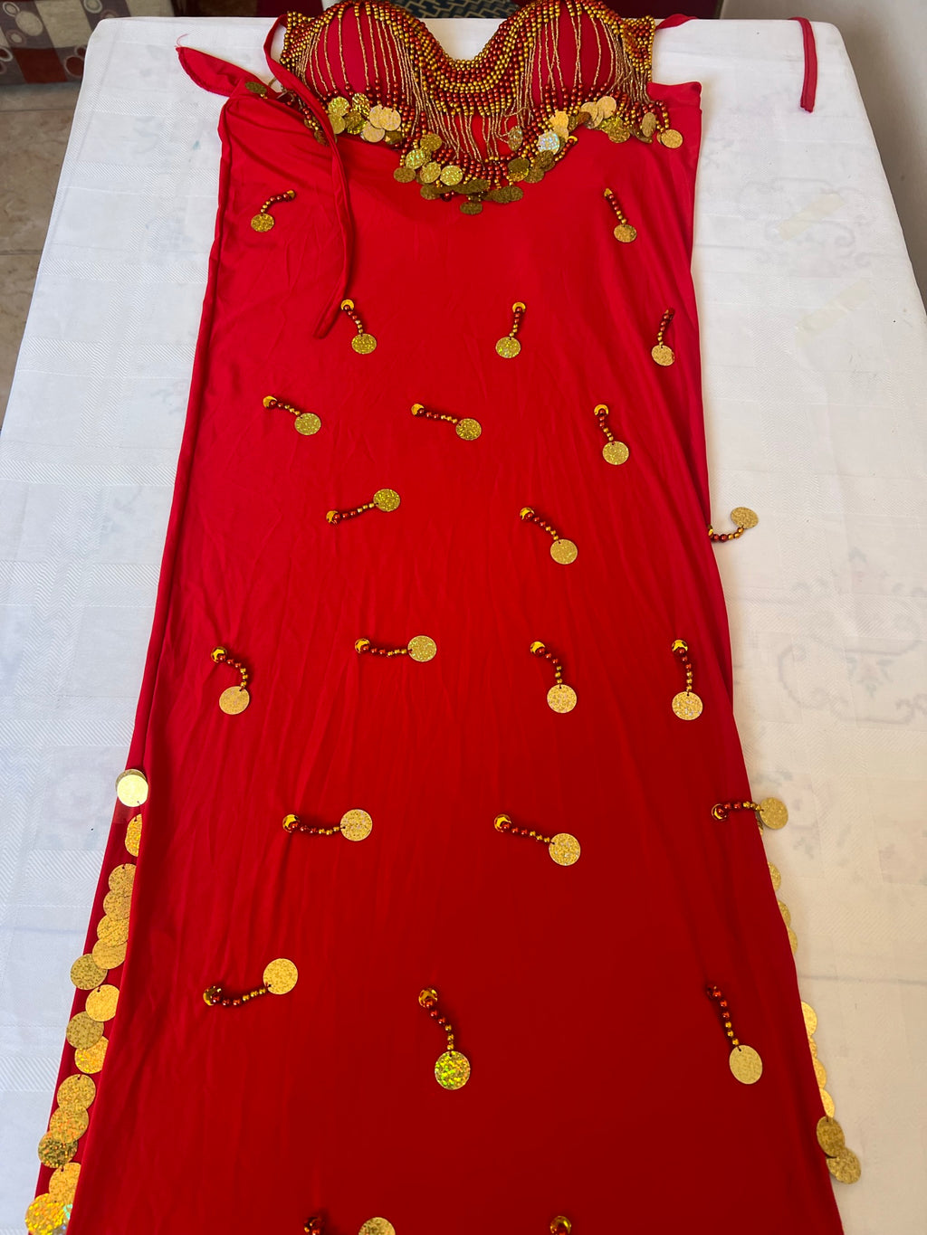 A red belly dance costume with handmade embroidered details and large sequins, laid out on a white surface.