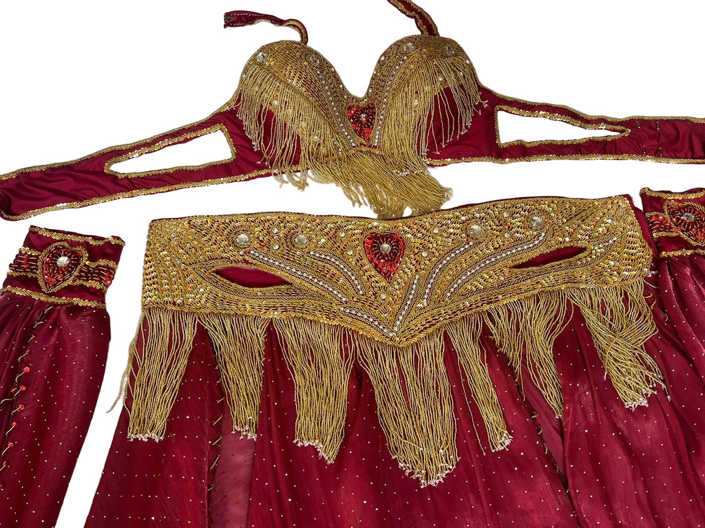 Decorative gold and red belly dance costume with intricate patterns and tassels on a textured white background