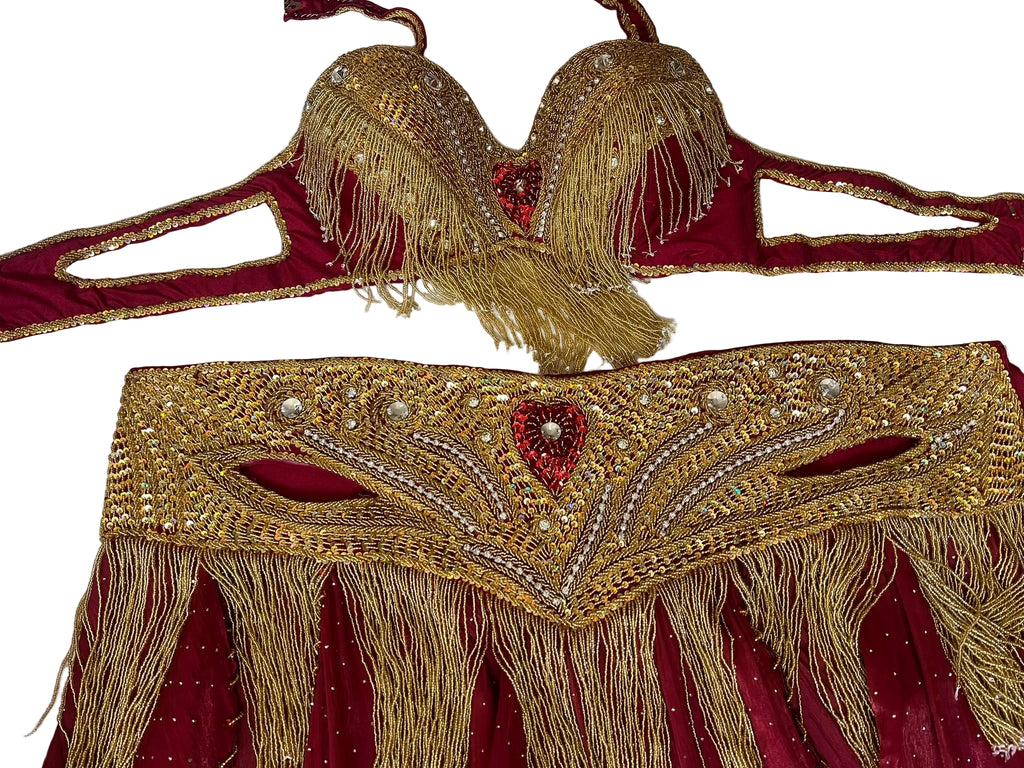 Decorative gold and red belly dance belt and bra with intricate patterns on a textured white background