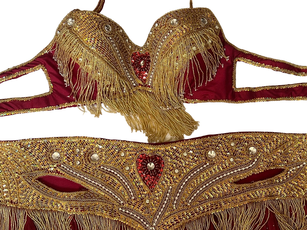 Decorative red and gold belly dance set with intricate patterns on a textured white background