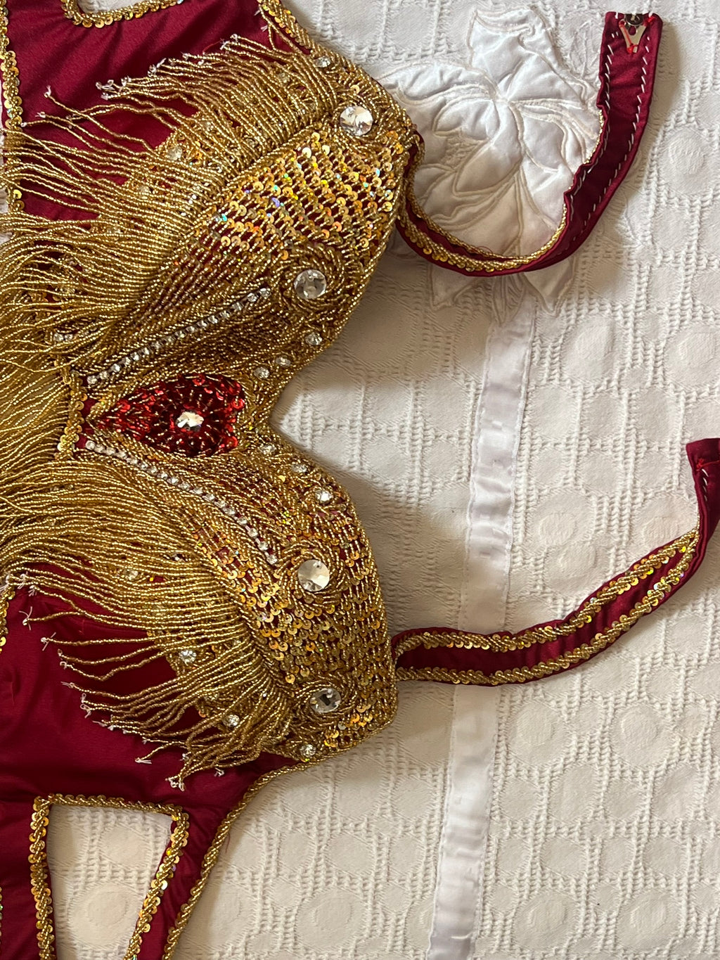 Decorative belly dance bra with gold fringe and red accents on a textured white background