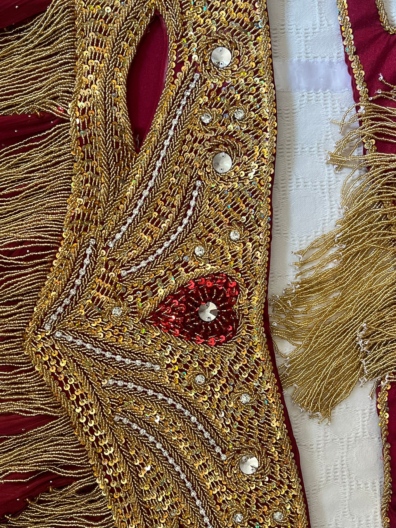 Close-up of a decorative Belly dance belt  with gold embroidery, red stones, and tassels on a white background.