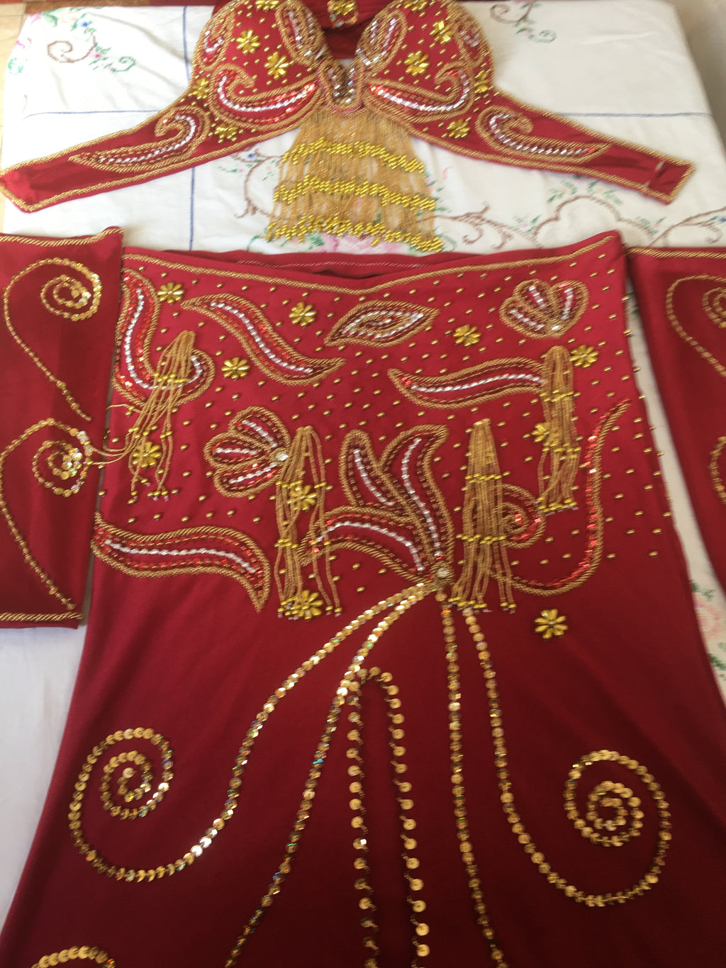 A professional red belly dance costume with gold, silver, and multicolored bead embellishments, including a skirt with a front slit, a bra, a chiffon veil, a pair of sleeves, and a headband.