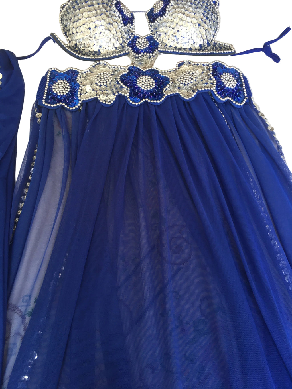 A close-up of a blue belly dance costume featuring intricate embellishments and a sheer fabric.