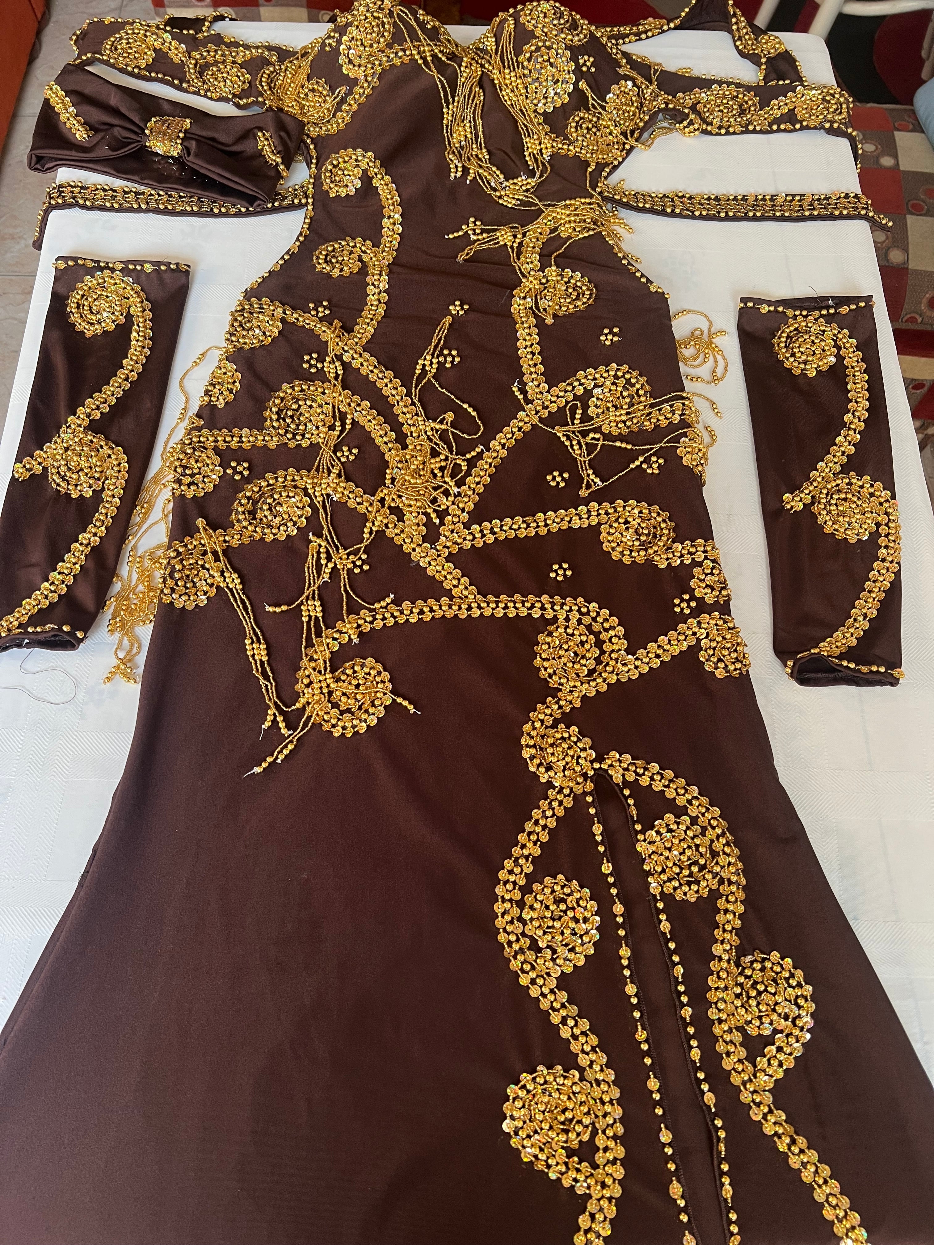 A brown belly dance costume with handmade embroidered details, including a skirt, bra, and sleeves, adorned with gold sequins and glass beads.