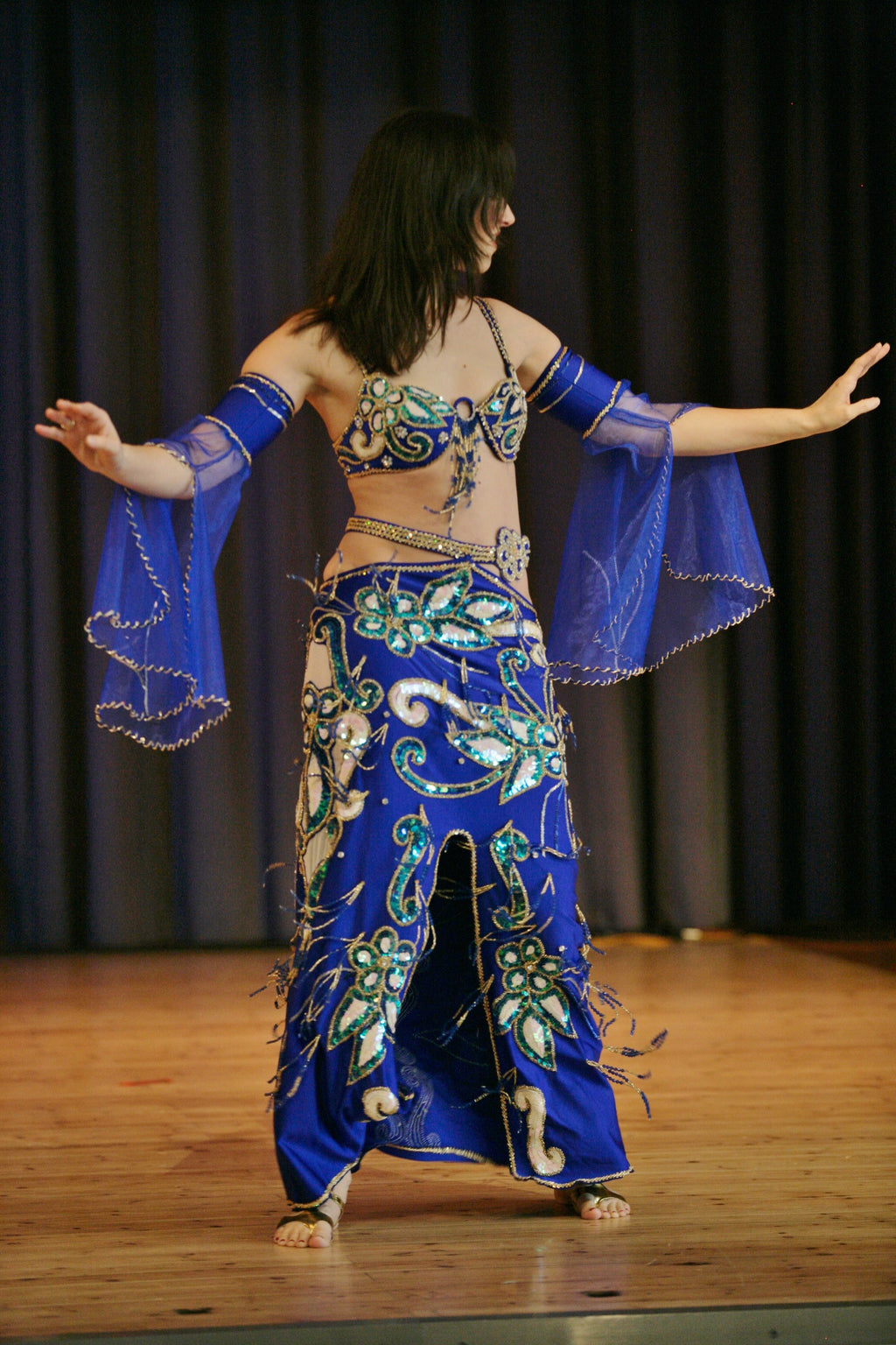 A woman performing a dance wearing a traditional blue belly dance costume with decorative elements.