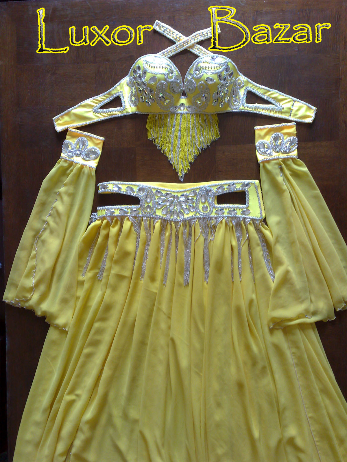 A professional belly dance costume featuring a yellow double-layer chiffon skirt with decorations, a matching bra, belt, and a pair of sleeves, all displayed on a flat surface.