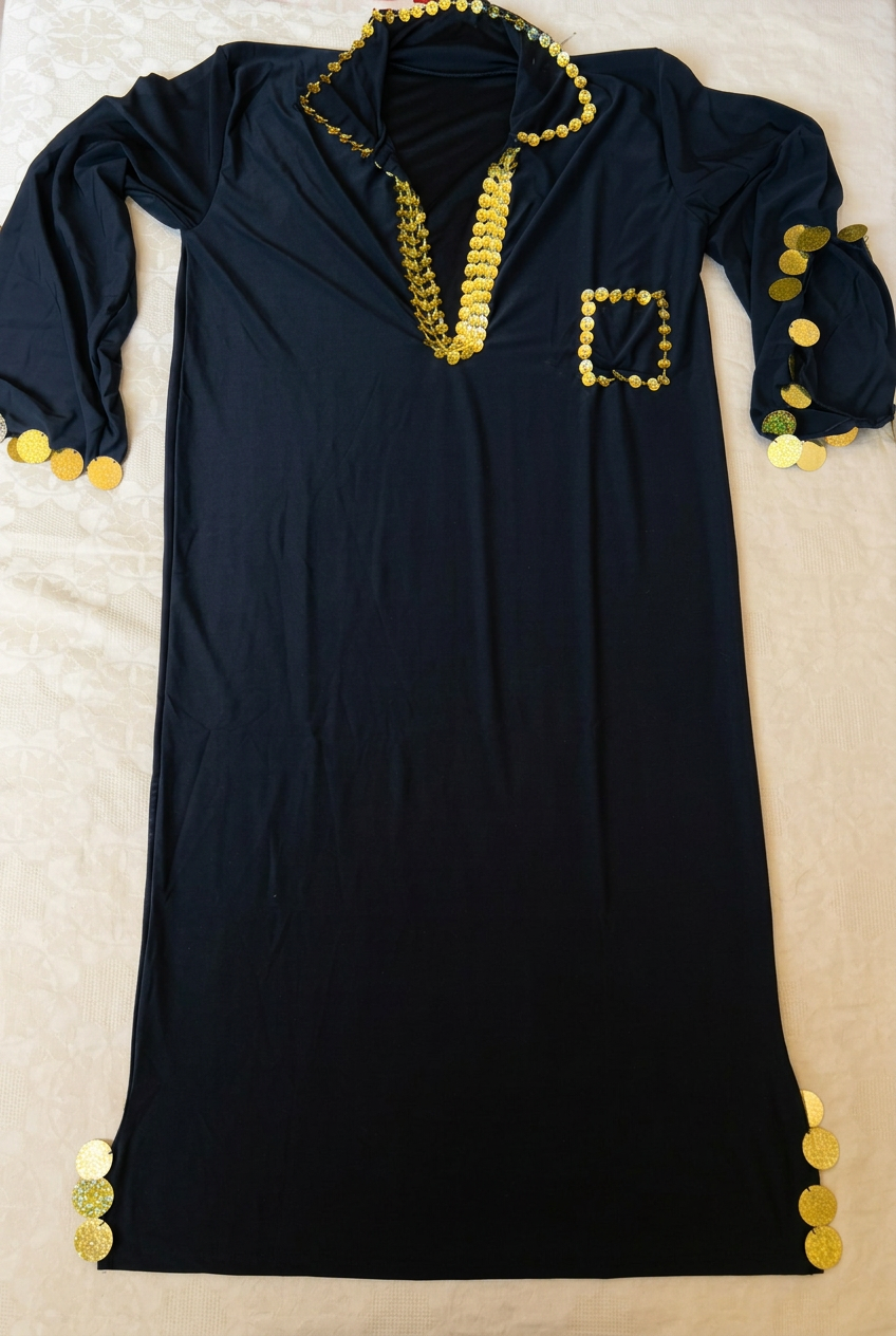Black Saidi belly dance dress laid flat on a beige surface, with gold-tone sequin trim around the neckline, pocket, sleeves and side slits.
