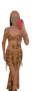 Person wearing a gold and beige belly dance outfit with intricate designs in a room.
