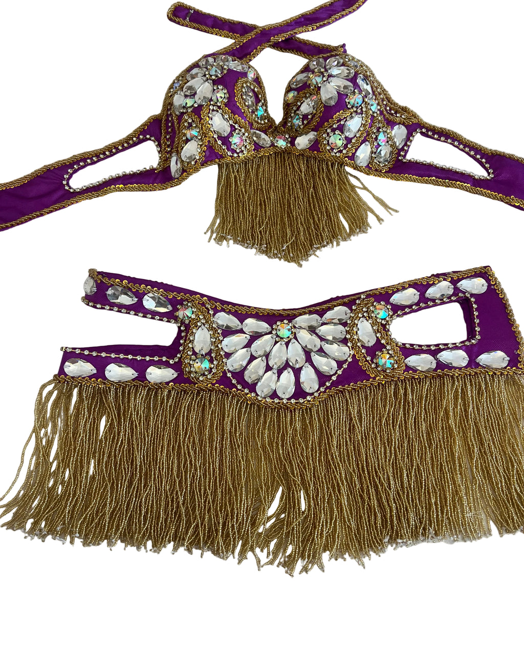 Purple belly dance costume set with gold fringe and white shell embellishments, laid flat on a white checkered surface.
