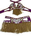 Purple belly dance costume set with gold fringe and white shell embellishments, laid flat on a white checkered surface.